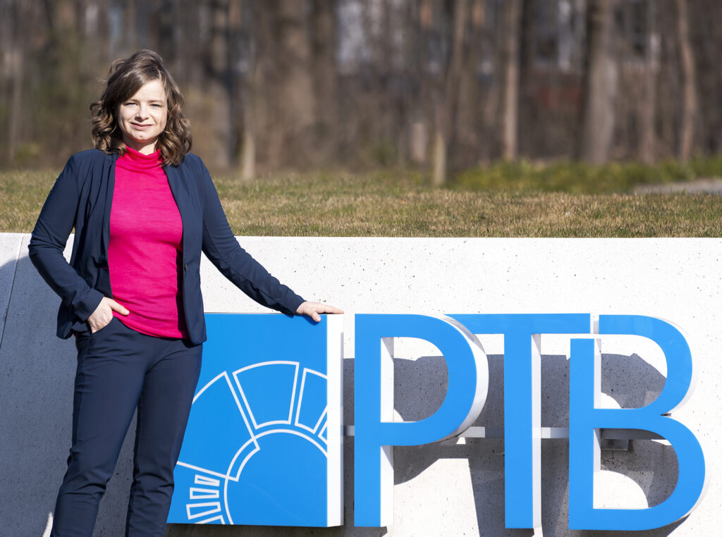 Anna Schätzlein stands at the PTB sign at the entrance to the site in Braunschweig.