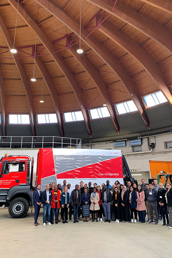 A group of people in front of a red truck with the inscription "Landesamt für Mess- und Eichwesen"