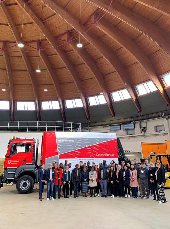 A group of people in front of a red truck with the inscription "Landesamt für Mess- und Eichwesen"