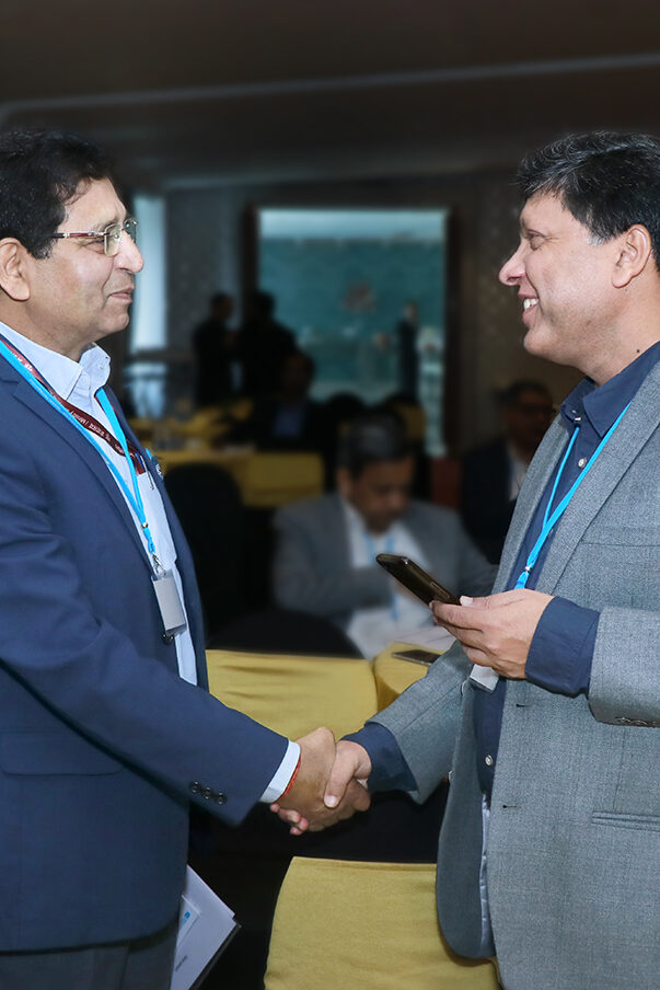 Two men are shaking hands and smiling at each other, on the left is Dr. A K Tripathi, Adviser to the Ministry of New and Renewable Energy and to the right is Dr. Sushil Kumar, National Physics Laboratory of India. In the background more people can be seen sitting and standing.