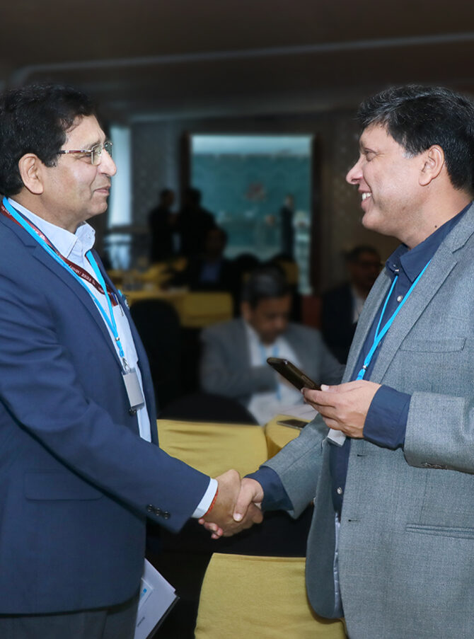 Two men are shaking hands and smiling at each other, on the left is Dr. A K Tripathi, Adviser to the Ministry of New and Renewable Energy and to the right is Dr. Sushil Kumar, National Physics Laboratory of India. In the background more people can be seen sitting and standing.
