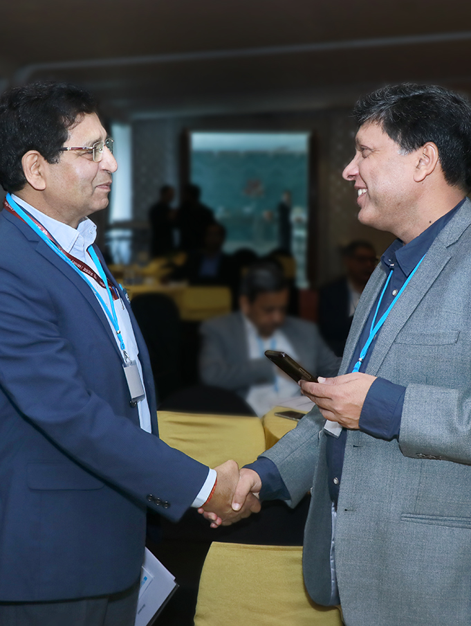 Two men are shaking hands and smiling at each other, on the left is Dr. A K Tripathi, Adviser to the Ministry of New and Renewable Energy and to the right is Dr. Sushil Kumar, National Physics Laboratory of India. In the background more people can be seen sitting and standing.