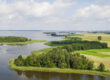 Photo of the Masurian Lake District in Poland. You can see a wide lake landscape with green shores and trees.