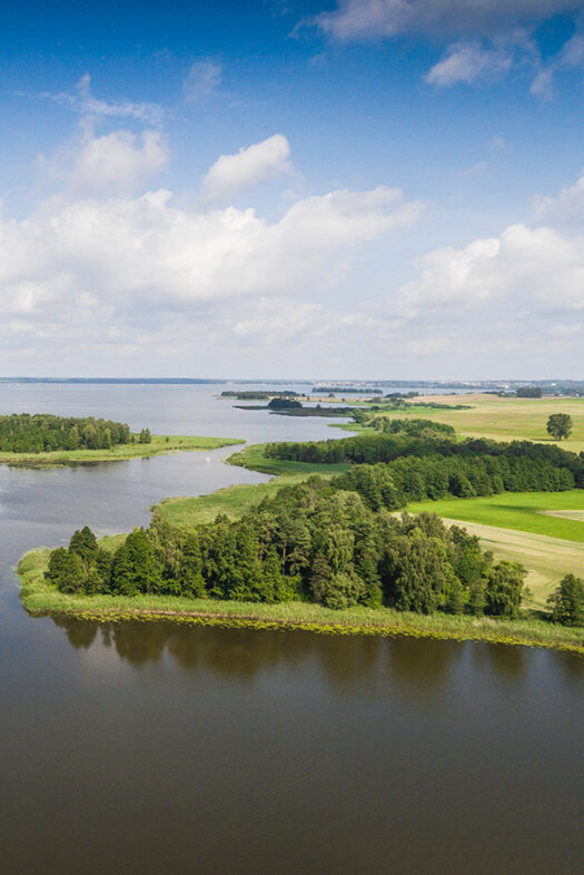 Photo of the Masurian Lake District in Poland. You can see a wide lake landscape with green shores and trees.