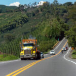 Un camión amarillo, cuatro coches y una moto circulan por una carretera rural en Colombia