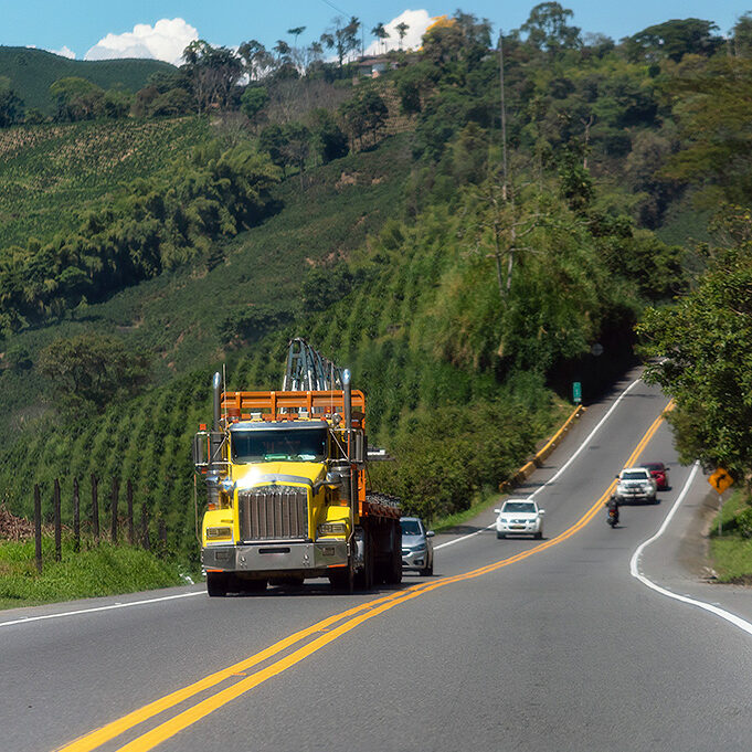 A yellow truck, four cars and a motorbike drive along a country road in Colombia