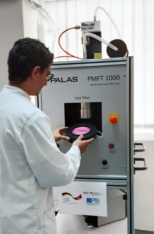 Laborkraft setzt rosafarbene Alltagsmaske in Prüfgerät ein.