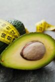 Avocado half and whole with tape measure on black background.