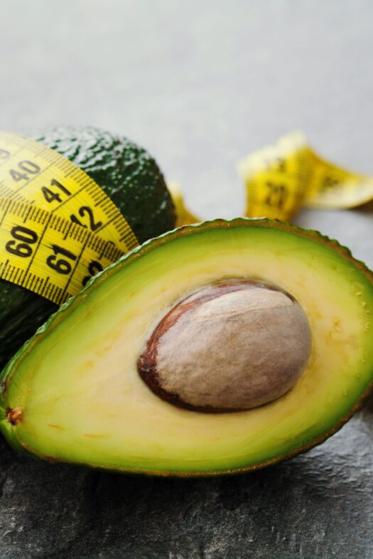 Avocado half and whole with tape measure on black background, diet concept