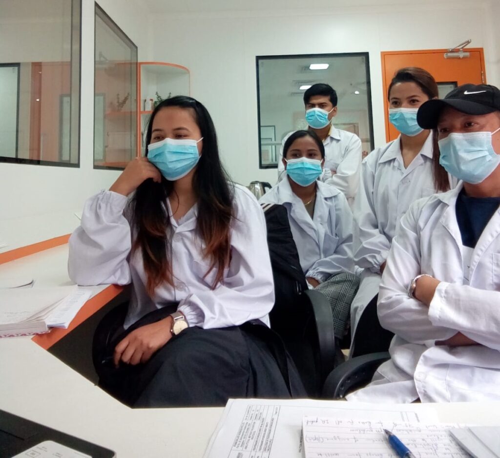 Participants of the virtual training of trainers seminar sit in front of a laptop with face masks and in medical professional clothing.