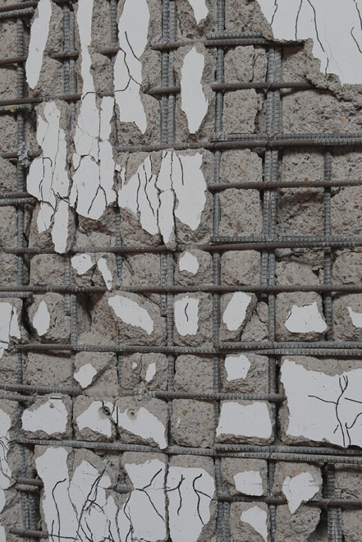 Eine brüchige Wand aus Beton, die von Stahlstangen durchzogen ist.