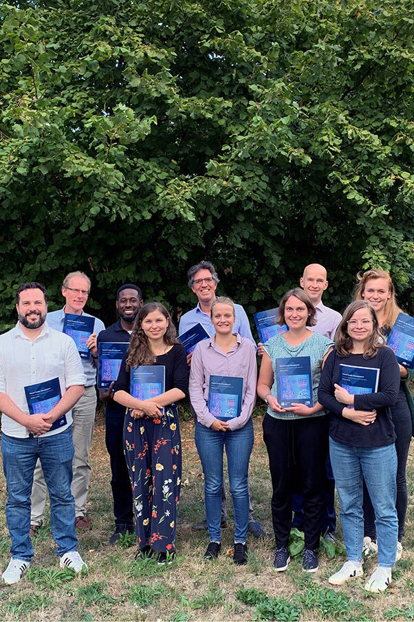 A group of workshop participants in front of green bushes.