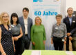 Four women and two men are standing in front of a poster which reads “60 years of technical cooperation”.