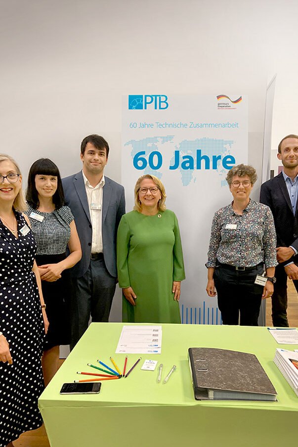 Four women and two men are standing in front of a poster which reads “60 years of technical cooperation”.