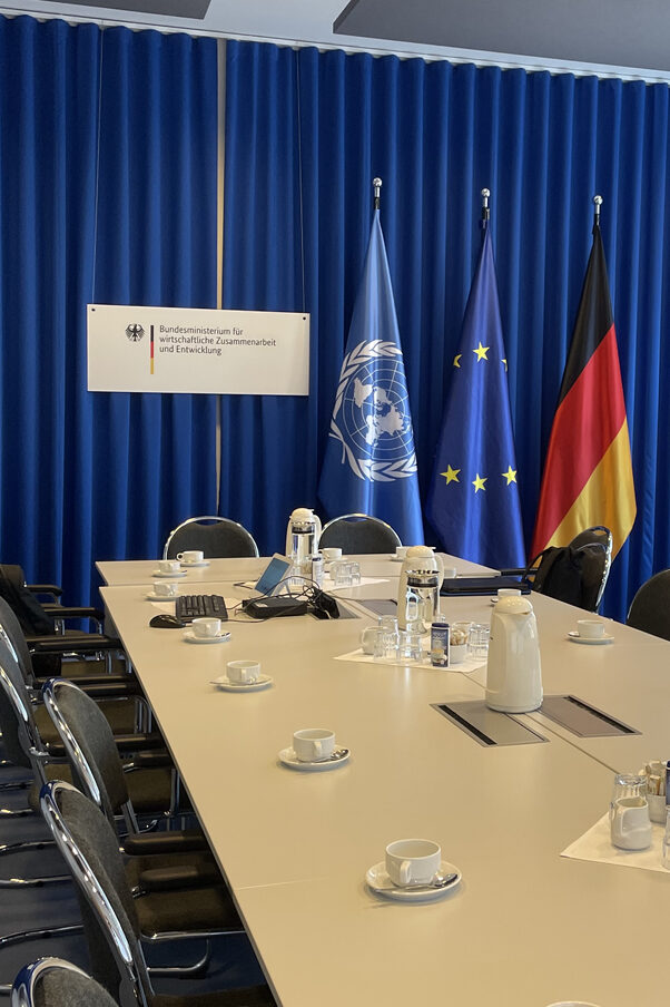 A conference room. Three flags are visible in the background.