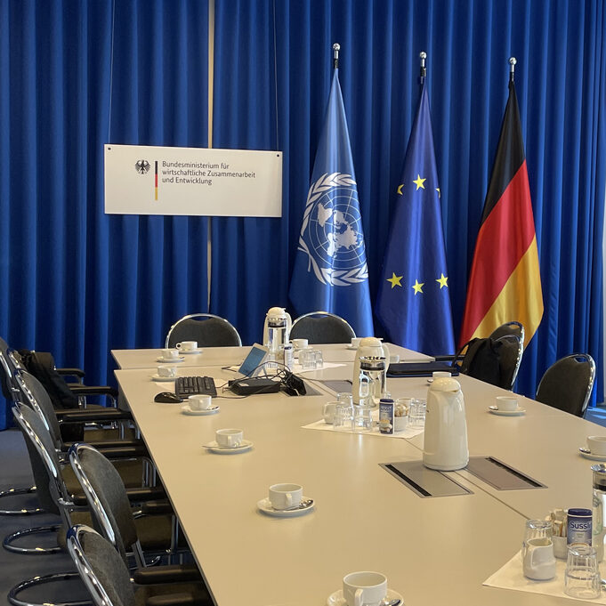 A conference room. Three flags are visible in the background.