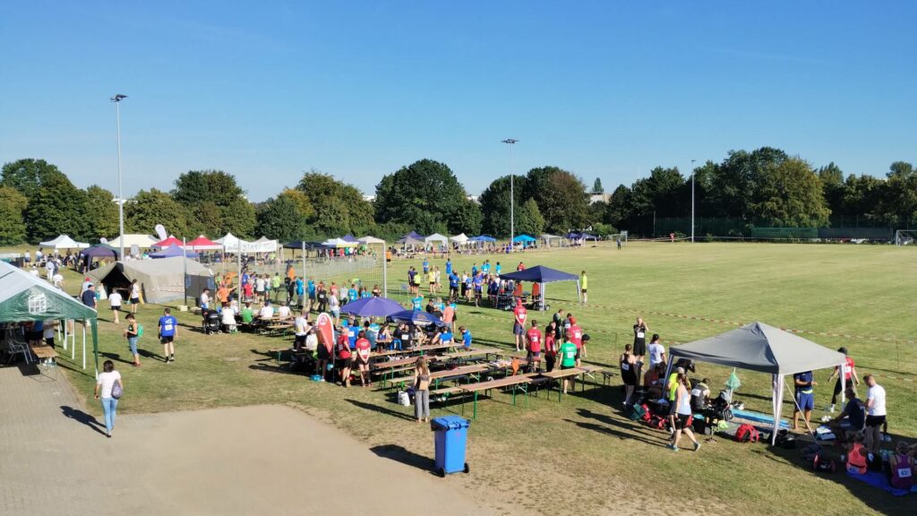 Panorama eines Sportplatzes. Viele Menschen stehen an Zelten und an der Laufstrecke.