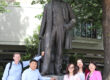 Two men and three women are standing next to a statue. The statue is of Werner von Siemens.