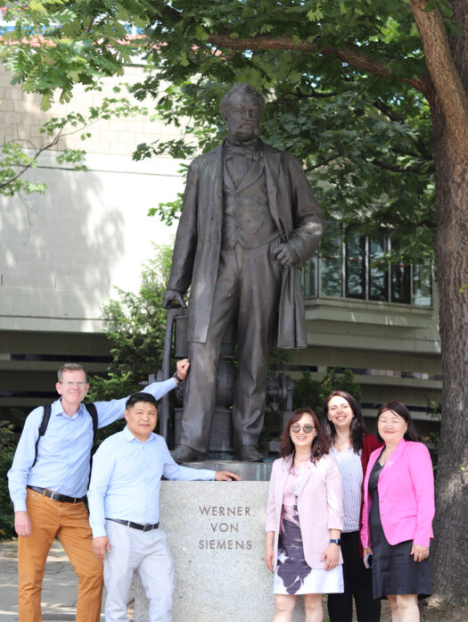 Vor einer Statue, die Werner von Siemens zeigt, stehen drei Frauen zur rechten und zwei Männer zur linken.