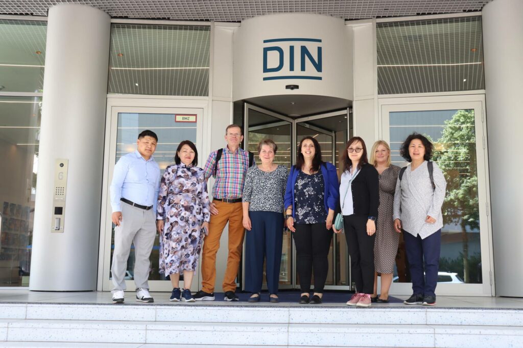 A group of people are standing in front of the entrance of a building. The name “DIN” is in capital letters above them.