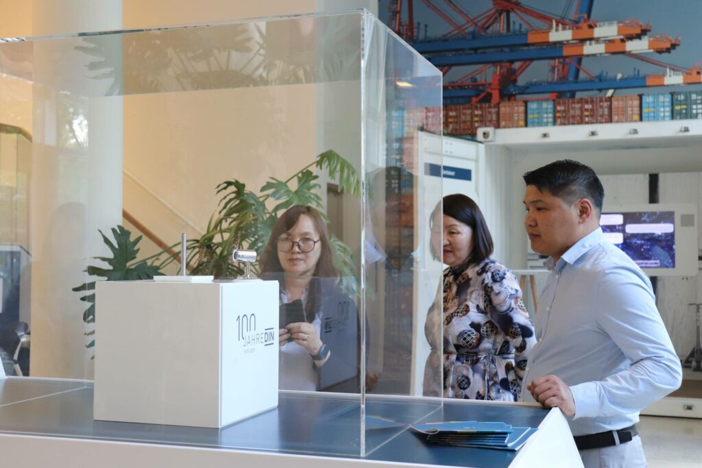 Two women and one man are standing behind a table with a glass display case containing an exhibit.