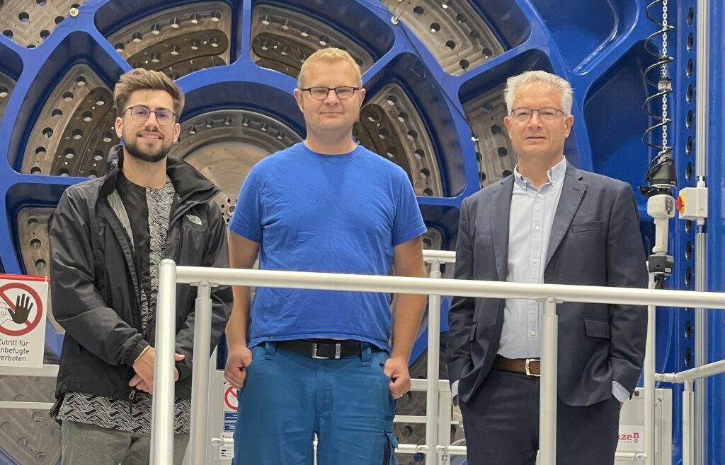 Three men standing in front of a huge machine