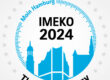 Die Beschriftungen ‚IMEKO 2024‘, ‚Think Metrology‘ sowie dem Slogan ‚Moin Hamburg‘ in einer kreisrunden Skala aus 25 Sternen mit einer stilisierten Ansicht von Hamburg. Die Sterne repräsentieren die 25 Technischen Komitees der IMEKO.