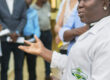 Eine Wissenschaftlerin, die einen Laborkittel der Ghana Standards Authority trägt, steht gestikulierend in einer Gruppe von Personen.