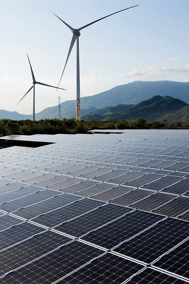 Solar photovoltaic panels and wind turbines in front of a mountain landscape
