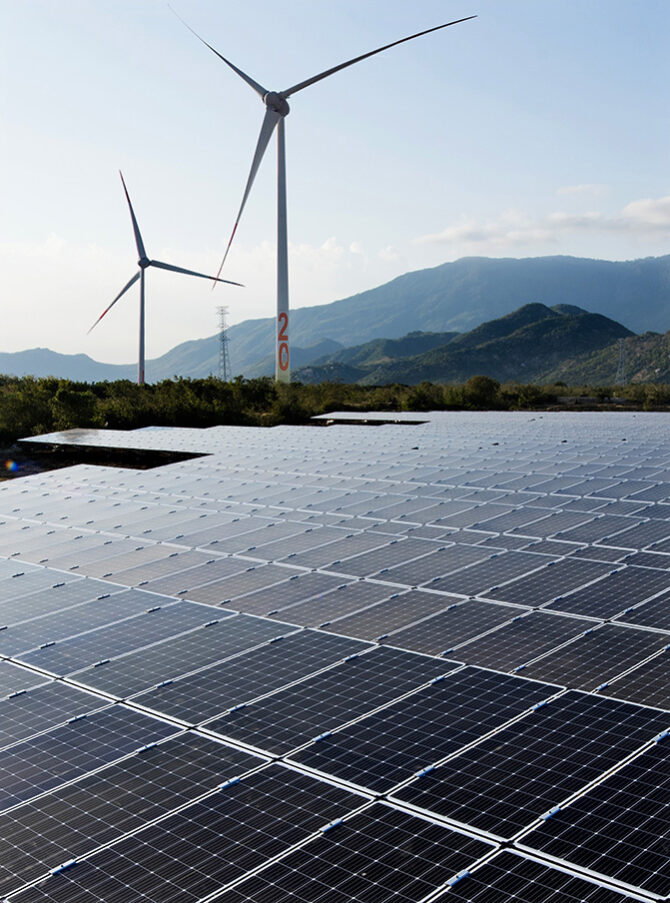 Solar photovoltaic panels and wind turbines in front of a mountain landscape