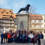 Eine Gruppe von Männern und Frauen steht vor dem Denkmal des Braunschweiger Löwen.