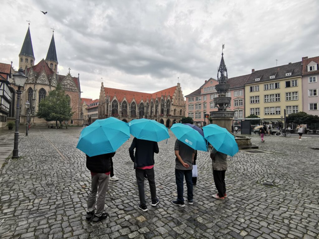 Four people with identical umbrellas stand on a large wet market square in front of medieval buildings