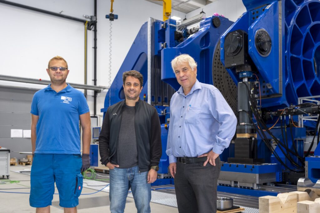 Three men standing in front of a large, blue machine.