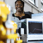 A woman standing behind research equipment for determining explosion pressure.