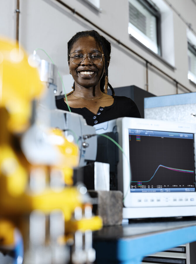 A woman standing behind research equipment for determining explosion pressure.