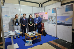 Four people are standing at an information booth in front of four roll-up banners, a display and information brochures.