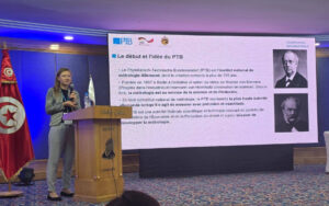 A person is standing at the podium on a stage, where a presentation of PTB’s history is shown in the middle of the picture.