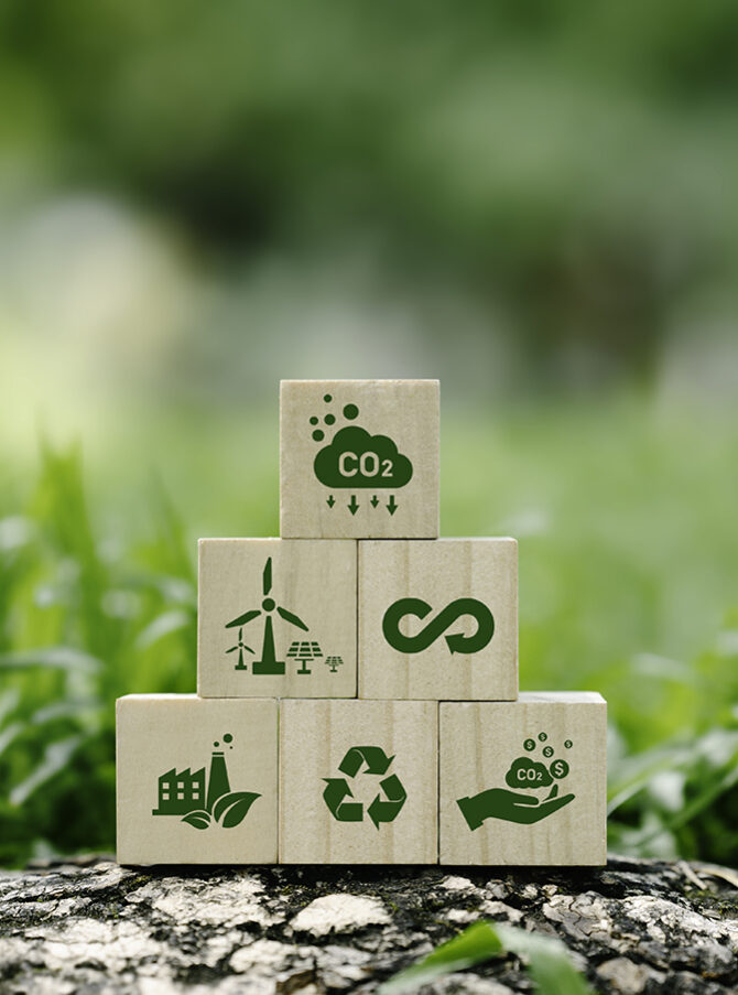 icon reduction of carbon emissions, carbon neutral, Net zero greenhouse gas emissions target, reducing carbon footprint concept, and CO2 emissions target on wooden cubes. circular economy concept A pyramid of wooden blocks displaying symbols such as windmills and recycling arrows with grass in the background.