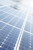Several solar modules at an angle are in the sun and reflecting light.