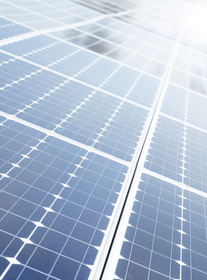 Several solar modules at an angle are in the sun and reflecting light.