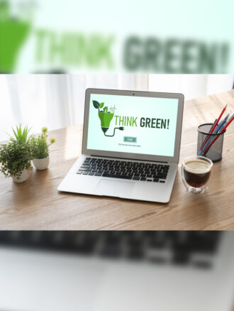 A laptop is on a wooden desk with three small plants, a cup of coffee, and a pencil cup. The computer screen says “Think Green!”