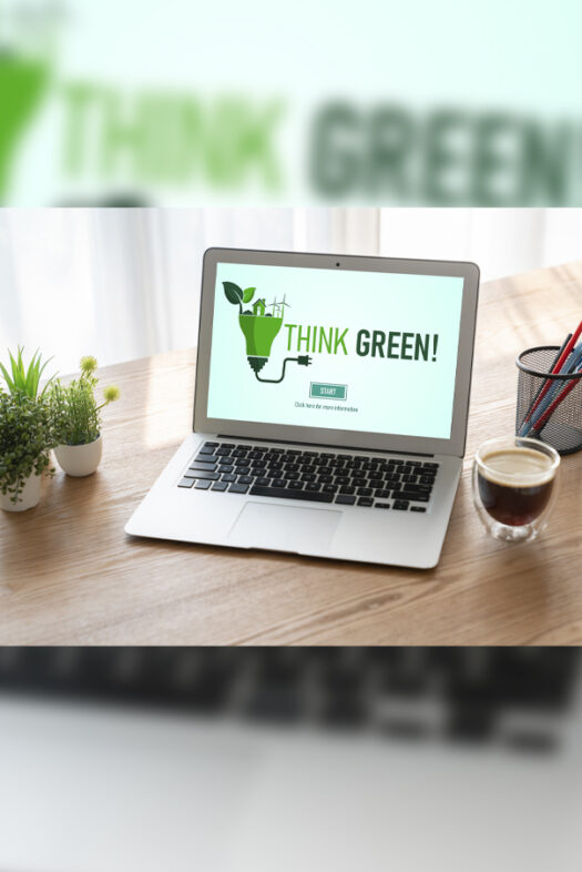 A laptop is on a wooden desk with three small plants, a cup of coffee, and a pencil cup. The computer screen says “Think Green!”