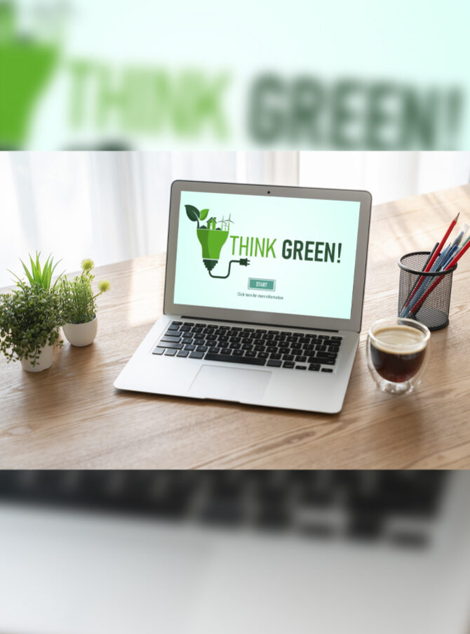 A laptop is on a wooden desk with three small plants, a cup of coffee, and a pencil cup. The computer screen says “Think Green!”