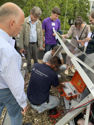 A group of people are gathered around a technician who is inspecting a PV module.