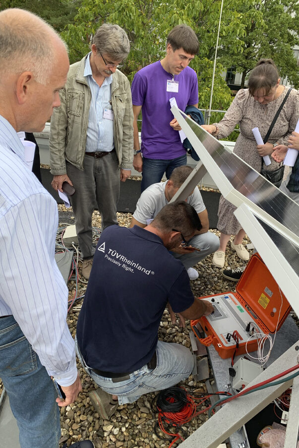 A group of people are gathered around a technician who is inspecting a PV module.