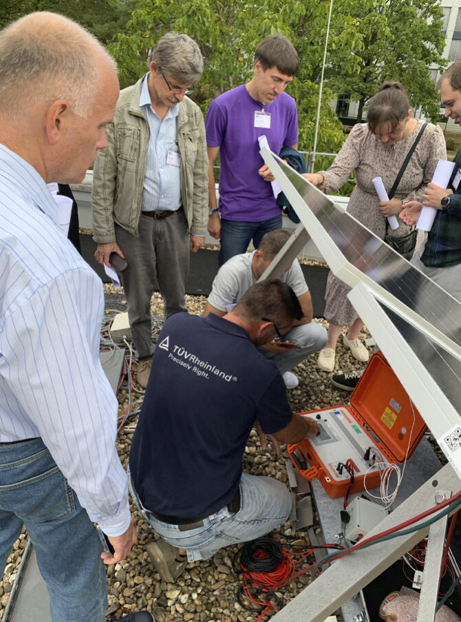 A group of people are gathered around a technician who is inspecting a PV module.